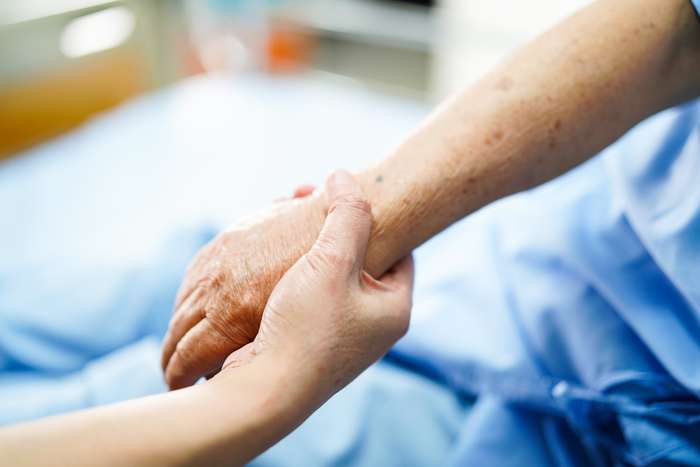 A caregiver holds the wrist of a patient in a hospital setting.
