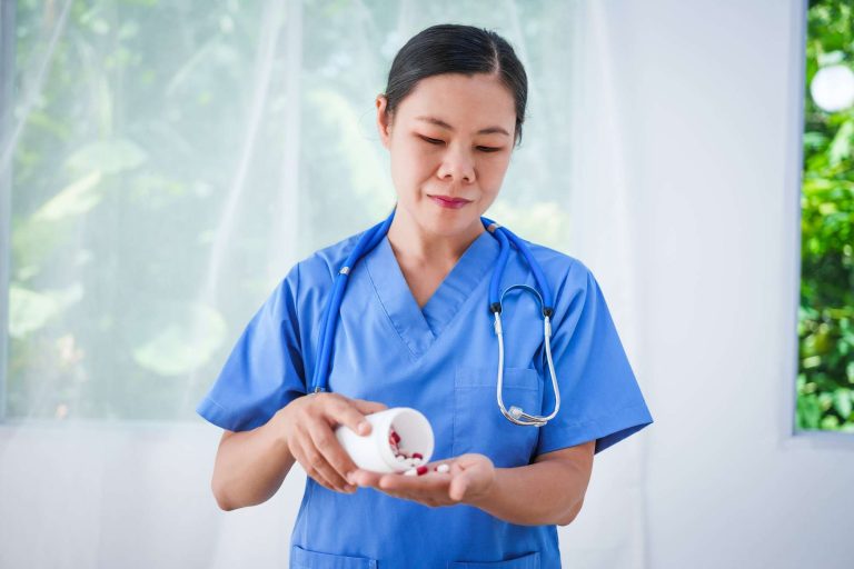 A healthcare professional in scrubs pours pills from a container into their hand.