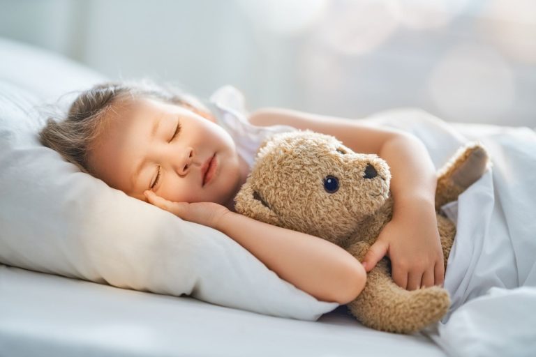 A young girl peacefully sleeps in bed while holding a teddy bear.