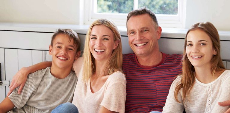 A smiling family of four sits together on a couch, enjoying each other's company.