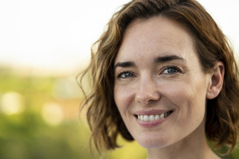 Smiling woman with curly hair against a blurred outdoor background.