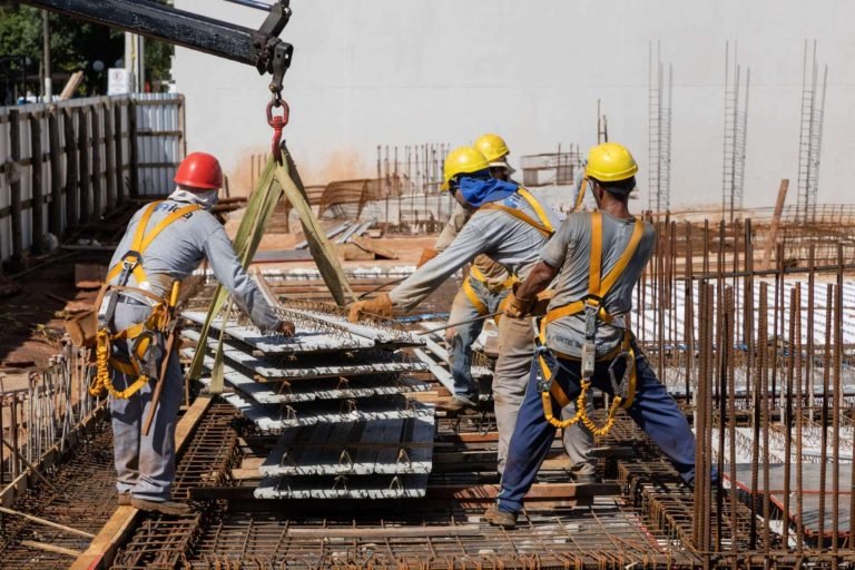Construction workers in safety gear maneuvering concrete slabs on a building site.