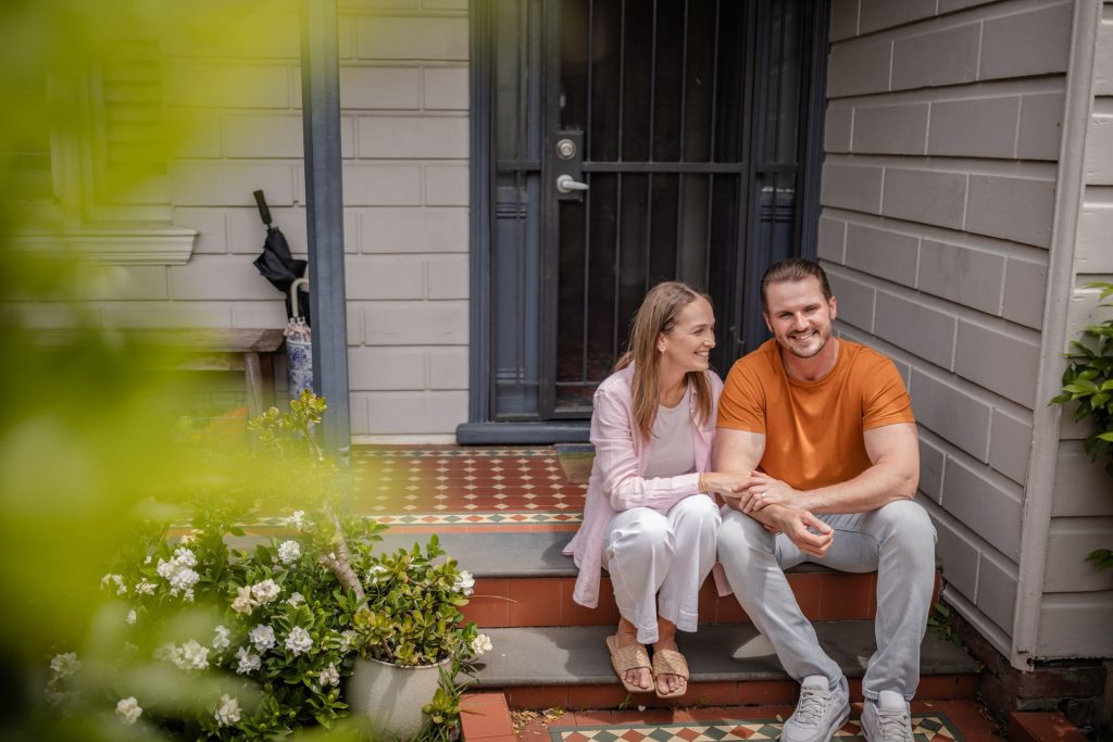 A couple sits together on the steps of a house, smiling and enjoying each other's company.