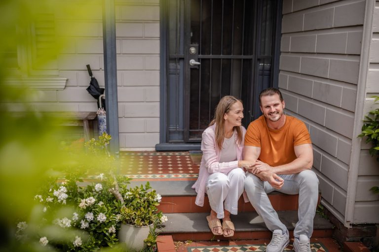 A couple sits together on the steps of a house, smiling and enjoying each other's company.